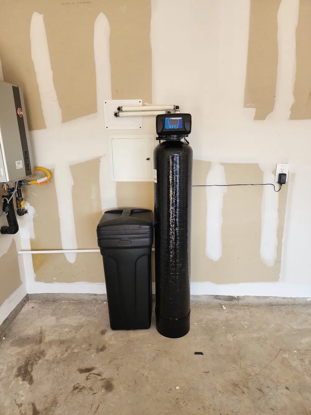 Softener and brine tank set against a garage wall next to a tankless water heater