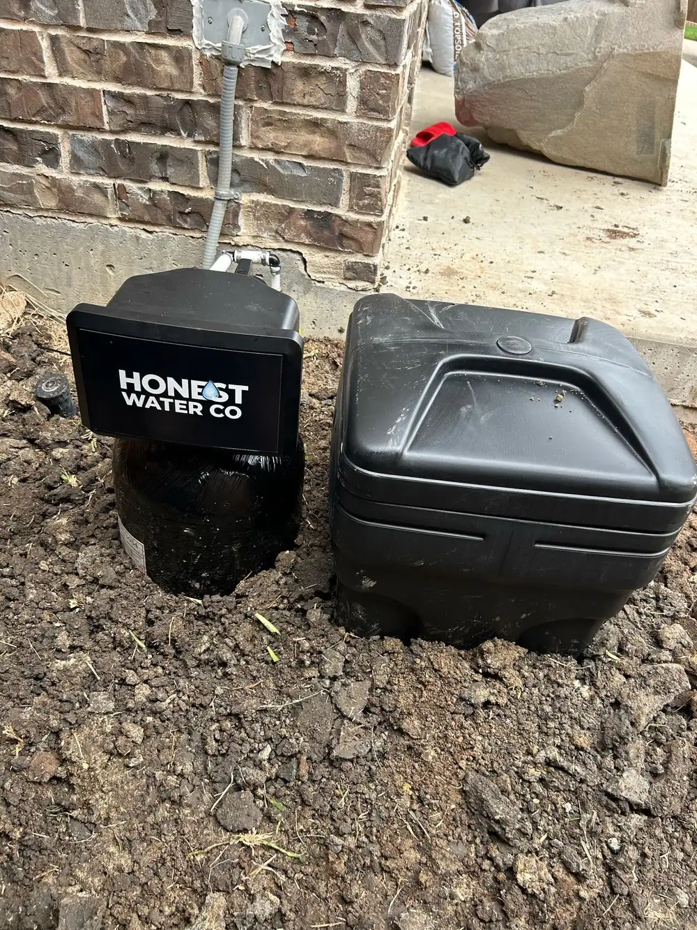 Exterior installation with the control head and brine tank set on grade beside a brick wall